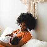 Tender moment of a mother with afro hair cradling her baby at home, showcasing love and warmth.
