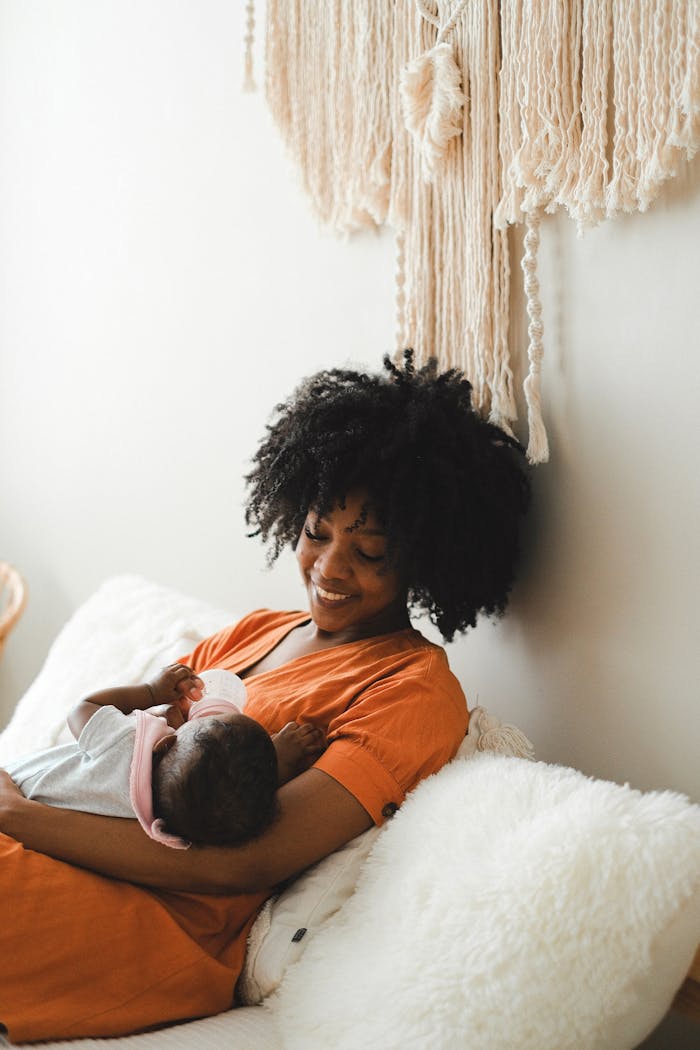 Tender moment of a mother with afro hair cradling her baby at home, showcasing love and warmth.