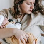 A mother lovingly cradles her sleeping newborn indoors, showcasing warmth and affection.